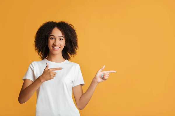 Az emberek őszinte érzelmek, életmód és a legjobb választás koncepciója. Vidám afro-amerikai hölgy fehér pólóban ujjal mutogat az üres tér felé. — Stock Fotó