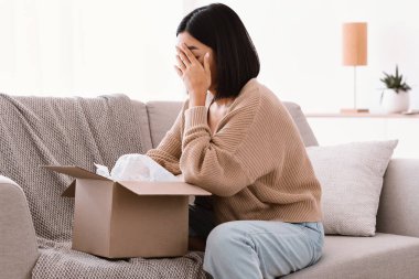 Üzgün genç kadın yanlış paketi açıyor, teslimat hatası.
