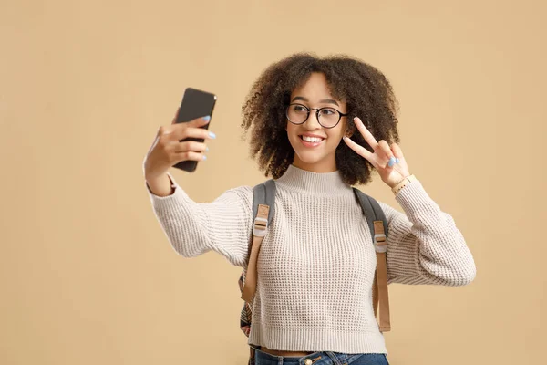 Selfie för personlig blogg om mode och utbildning. Leende afrikansk amerikansk kvinna i glasögon gör fred tecken och ta foto — Stockfoto