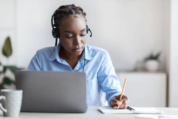 Онлайн-навчання. Чорна жінка-працівник дивиться вебінар на ноутбук і робить нотатки — стокове фото