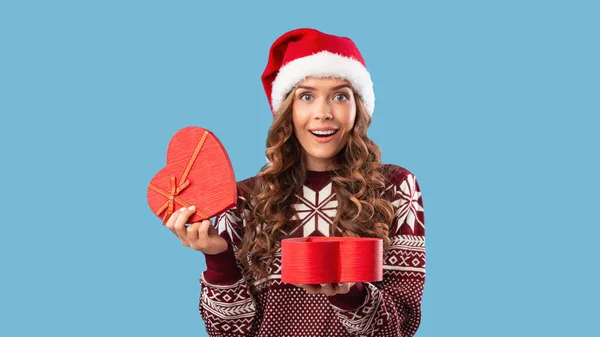 Sorpresa de Navidad. Preciosa mujer milenaria en Santa sombrero apertura corazón en forma de caja de regalo en fondo de estudio azul — Foto de Stock