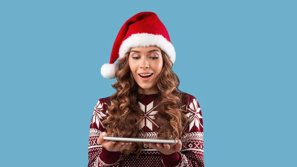 Encantadora dama milenaria en traje de invierno con tableta sorprendida por la enorme venta de Navidad en la tienda en línea sobre fondo azul — Foto de Stock