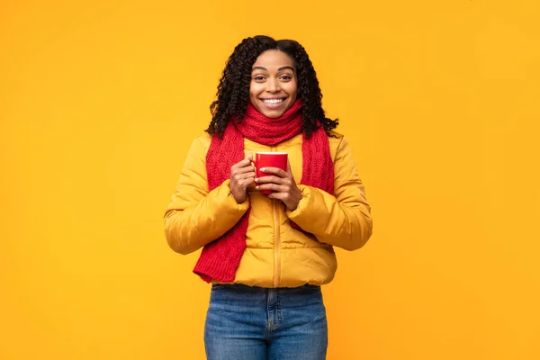 Μαύρη γυναίκα στο Χειμώνα Jacket Holding Κύπελλο καφέ, κίτρινο φόντο — Φωτογραφία Αρχείου