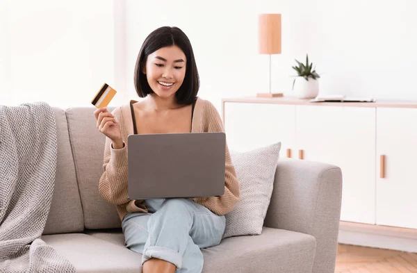 Young asian woman making purchases sitting with pc on sofa — Stock Photo, Image