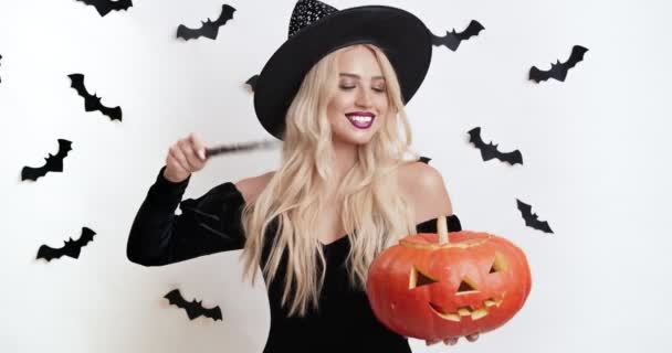 Krásná čarodějka čarování s kouzelnou hůlkou a vyřezávané Halloween dýně, dělat zázrak ve studiu — Stock video
