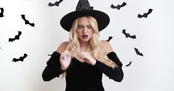 Недовольная молодая ведьма в черном костюме на Хэллоуин массирует виски, страдает головной болью — стоковое видео