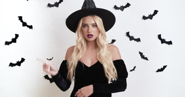 Seriösa unga Halloween häxa sätta fingret på läppar, gester för att vara tyst, vit med fladdermöss studio bakgrund — Stockvideo