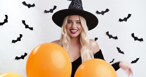 Boldog Halloweent! Gyönyörű fiatal pózol mágikus pálca és narancssárga lufik felett fehér stúdió háttér — Stock videók