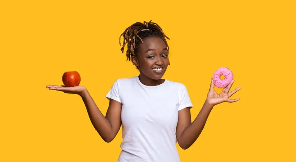Mosolygó fekete nő néz kamera, miután alma és fánk — Stock Fotó