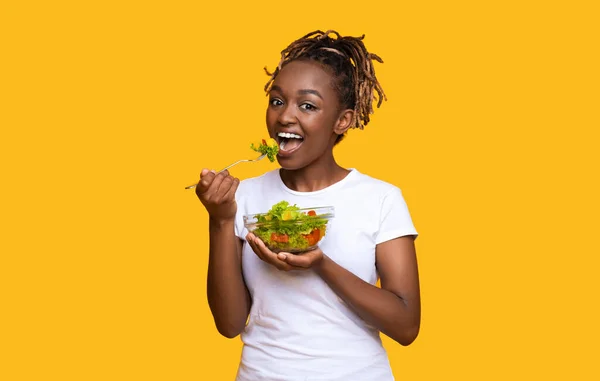 Healthy black lady eating fresh salad over yellow — Stock Photo, Image