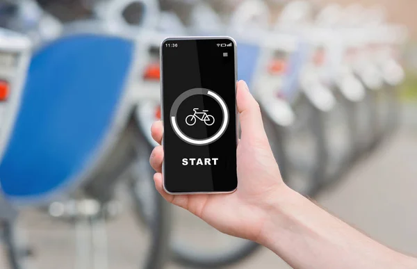 Moderno allenamento all'aperto con tecnologia e gita in bicicletta. Mano tiene il telefono con pulsante di avvio e bici sullo schermo — Foto Stock