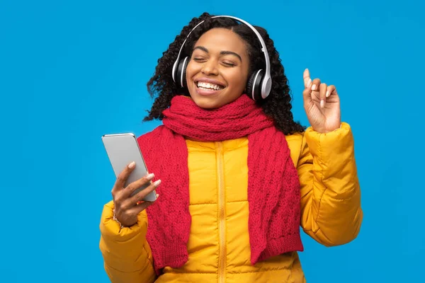 African Lady In Headphones Holding Smartphone Enjoying Music, Blue Background