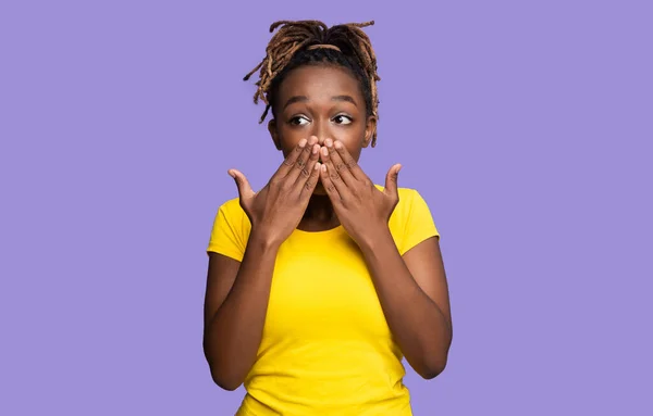 Счастливая эмоциональная черная женщина закрывает рот обеими ладонями — стоковое фото