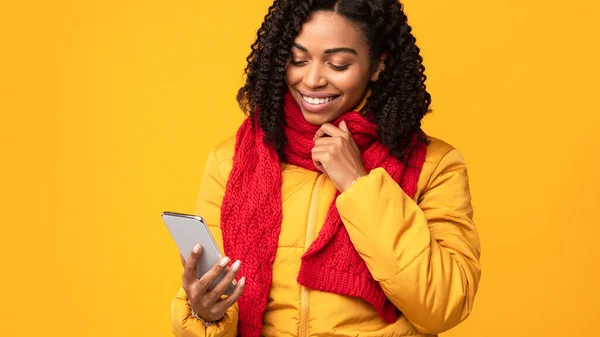 Μαύρη γυναίκα με κινητό τηλέφωνο ανάγνωση μηνυμάτων πάνω από κίτρινο φόντο — Φωτογραφία Αρχείου