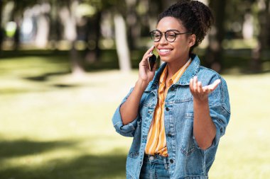 Neşeli siyahi kadın parkta cep telefonuyla konuşuyor.