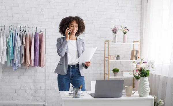 Lachende Afrikaans-Amerikaanse vrouw die documenten bekijkt en telefoneert in de woonkamer — Stockfoto