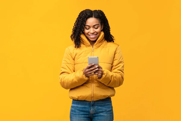 노란 배경 위에 서 있는 스마트 폰 문자를 가진 아프리카계 미국인 여성 — 스톡 사진