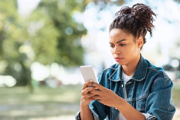 Mujer afroamericana descontenta usando lectura de teléfonos inteligentes Mensaje negativo al aire libre —  Fotos de Stock