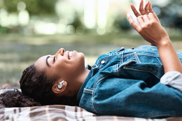 African Woman Słuchanie muzyki w słuchawki leżące na kratę na zewnątrz — Zdjęcie stockowe