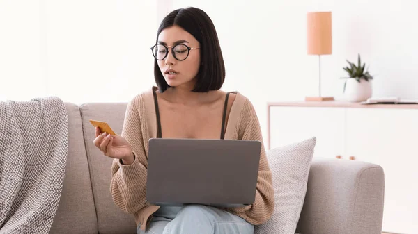 Young asian lady making purchases sitting with pc on couch — Stock Photo, Image