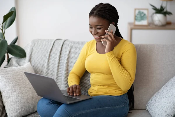 Távoli munka. Vidám afrikai nő dolgozik laptop és mobiltelefon otthon — Stock Fotó