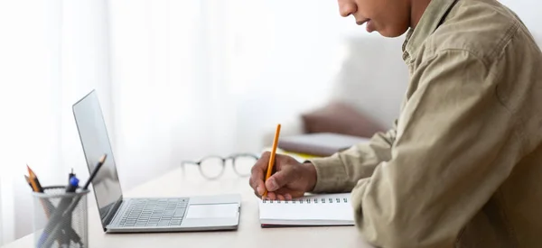 Webbbaserad utbildning. Närbild av svart manlig student skriver i copybook nära laptop hemma, banner design med kopieringsutrymme — Stockfoto