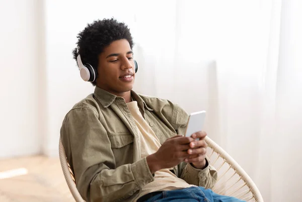 Atraente afro-americano cara em fones de ouvido desfrutando de grande música, ouvindo audiobook ou rádio no dispositivo móvel — Fotografia de Stock