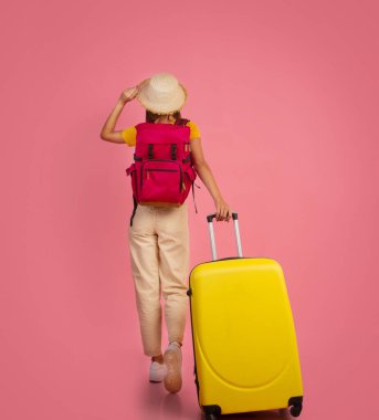 Pembe arka planda bavulu olan sırt çantalı kadın.