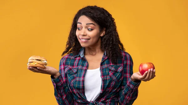 Hambre afroamericana dama sosteniendo hamburguesa y manzana fruta — Foto de Stock