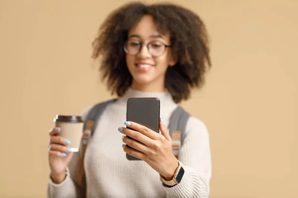 Fokus på smartphone med tomt utrymme i händerna på afrikansk amerikansk kvinna med ryggsäck och glasögon som håller kopp kaffe — Stockfoto
