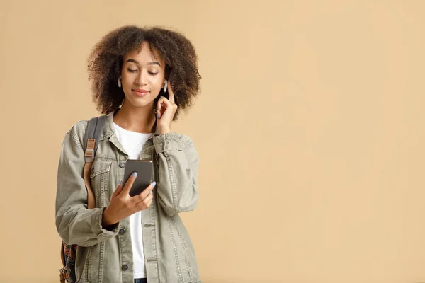 Moderna apparater för millennials. Lugn afrikansk amerikansk ung kvinna sätter på trådlösa hörlurar — Stockfoto