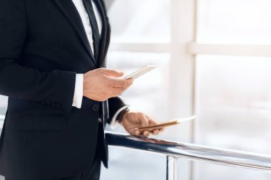 Bilinmeyen iş adamı akıllı telefon kullanıyor, elinde pasaport ve biletler var.