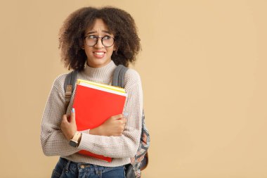 Gözlüklü, sırt çantalı ve akıllı saatli üzgün Afrikalı Amerikalı kadın not defteri tutuyor.