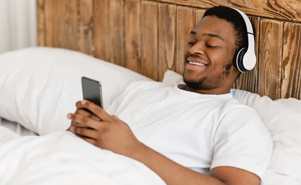 활기찬 흑인 남자가 침대에서 헤드폰을 들고 누워 있는 모습 — 스톡 사진