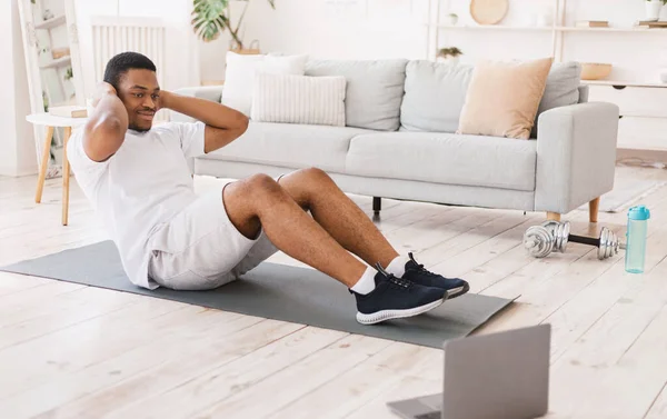 African Man Ćwiczenia robi przysiady Abs Ćwiczenia na laptopie w pomieszczeniach — Zdjęcie stockowe