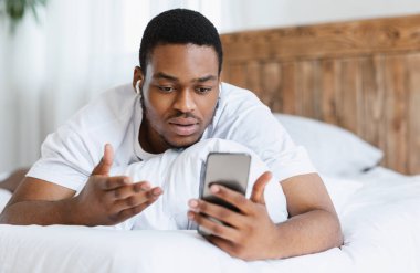 Ciddi Afrikalı Adam yatakta akıllı telefondan video görüşmesi yapıyor.