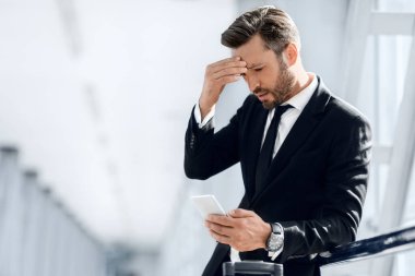 Havaalanının penceresinde duran yorgun işadamı, telefon kullanıyor.