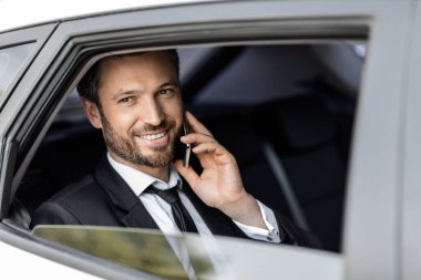 Arabayla giderken telefonla konuşan neşeli bir girişimci.