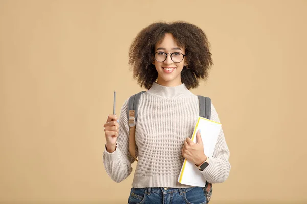 Wesoła Afroamerykanka w okularach, swetrze i notatniku podnosi pióro, izolowane na żółtym tle — Zdjęcie stockowe