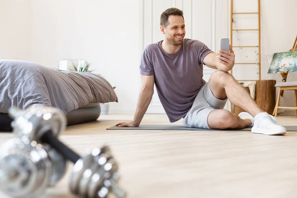 Uomo di formazione utilizzando Smartphone esercizio seduto sul tappetino a casa — Foto Stock