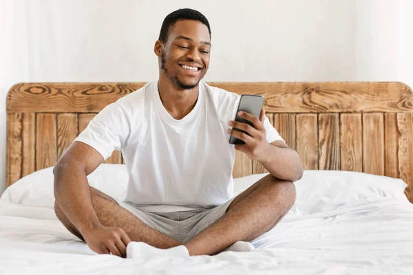 Μαύρος τύπος που χρησιμοποιεί το κινητό τηλέφωνο κάνει βιντεοκλήση κάθεται στο υπνοδωμάτιο — Φωτογραφία Αρχείου