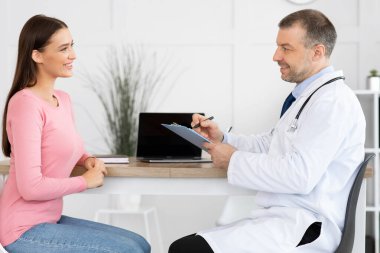 Erkek deneyimli doktor gülümseyen hastasıyla konuşuyor.