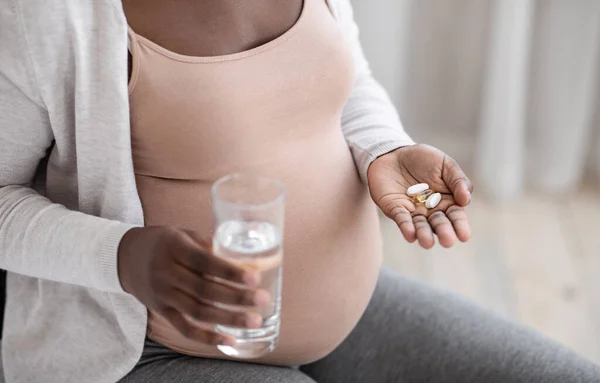 Vitaminer och kosttillskott. Oigenkännlig svart gravid kvinna som tar piller och vatten — Stockfoto