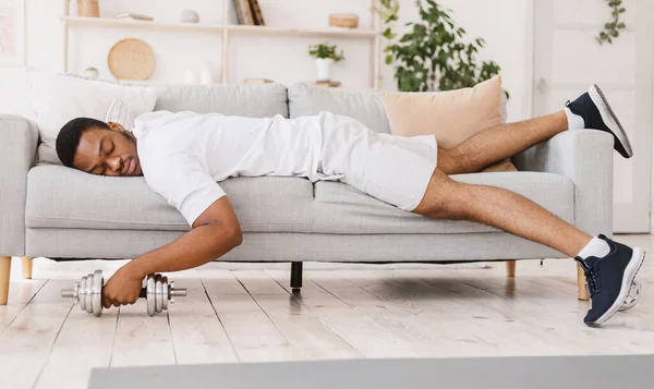 Uitgeputte zwarte man houden dumbbell slapen op de bank thuis — Stockfoto
