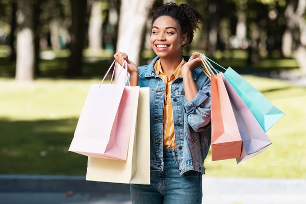 Feliz dama negra haciendo compras llevando bolsas de compras caminando al aire libre — Foto de Stock