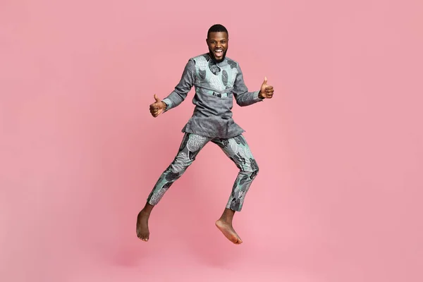 Joyful black guy showing thumbs up and jumping on pink