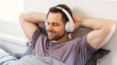 Evde yatağında kulaklık takmış, müzik dinleyen rahat bir adam.
