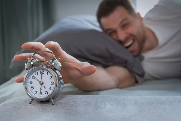 Boze man zet de wekker uit wakker worden liggend in bed — Stockfoto