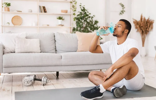 黑人在室内坐着锻炼身体时喝水 — 图库照片