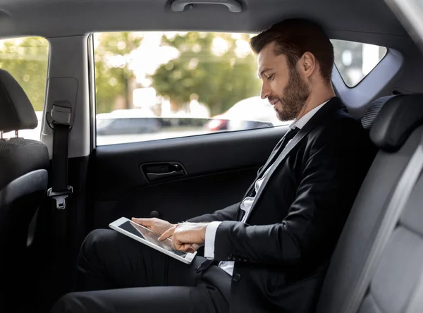 Wealthy man working on digital pad while going to airport